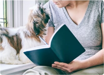 Egy nő jegyzeteket készít és közben a mellette álló kutyájára pillant.